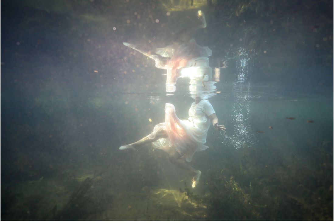 A woman wearing a white dress underwater in Allison Janae Hamilton's piece "Floridawater II, 2019."